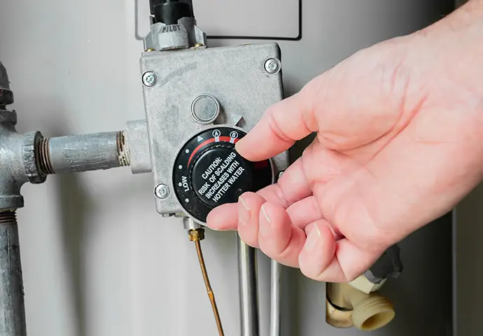 Technician adjusting the temperature control on a gas water heater.